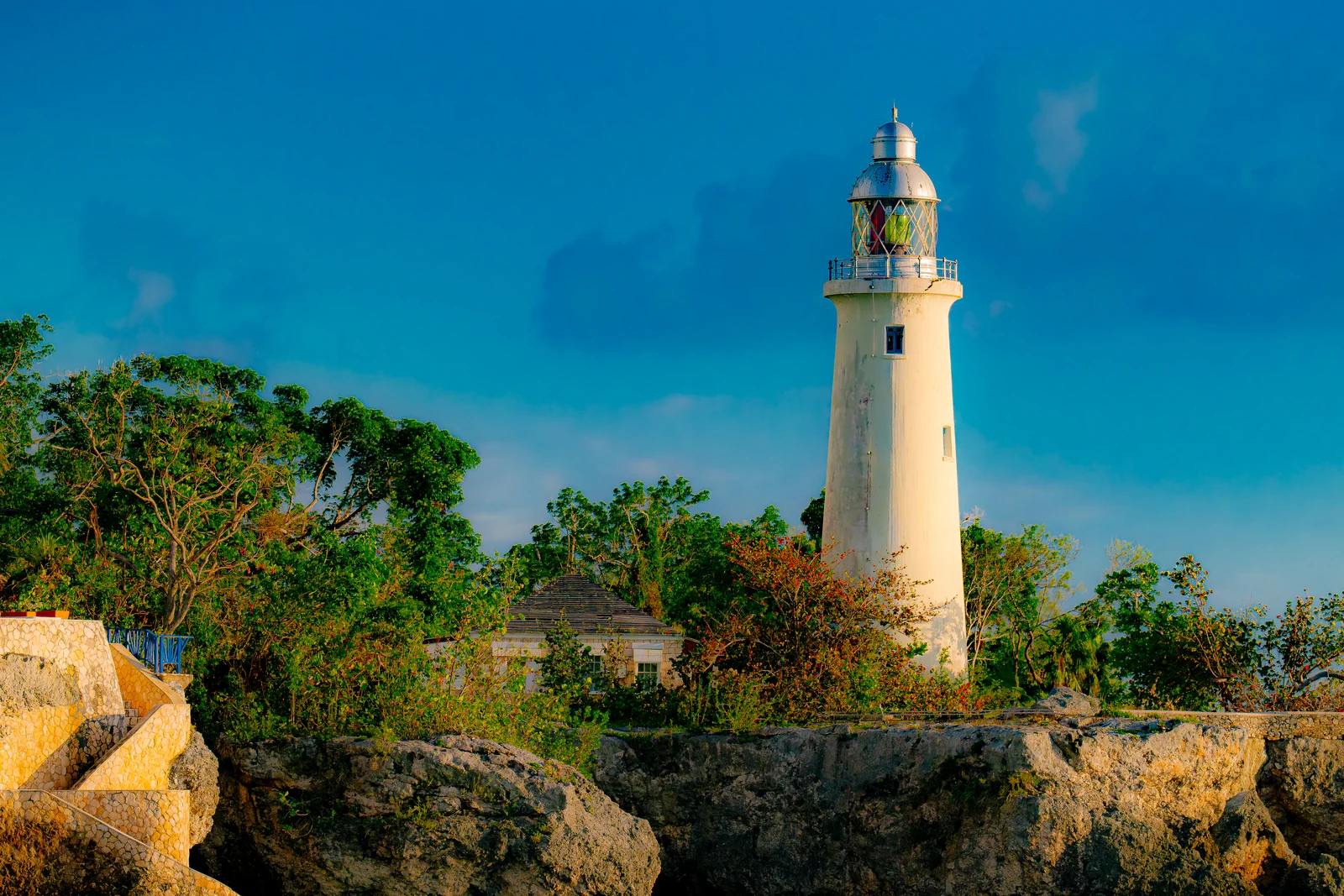 Negril Lighthouse in Jamaica rising above trees and limestone cliffs under a deep blue sky