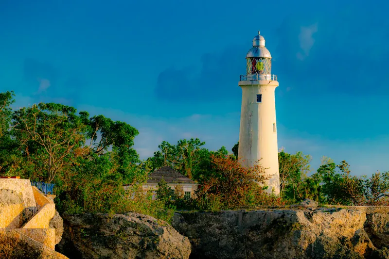 Negril Lighthouse in Jamaica rising above trees and limestone cliffs under a deep blue sky