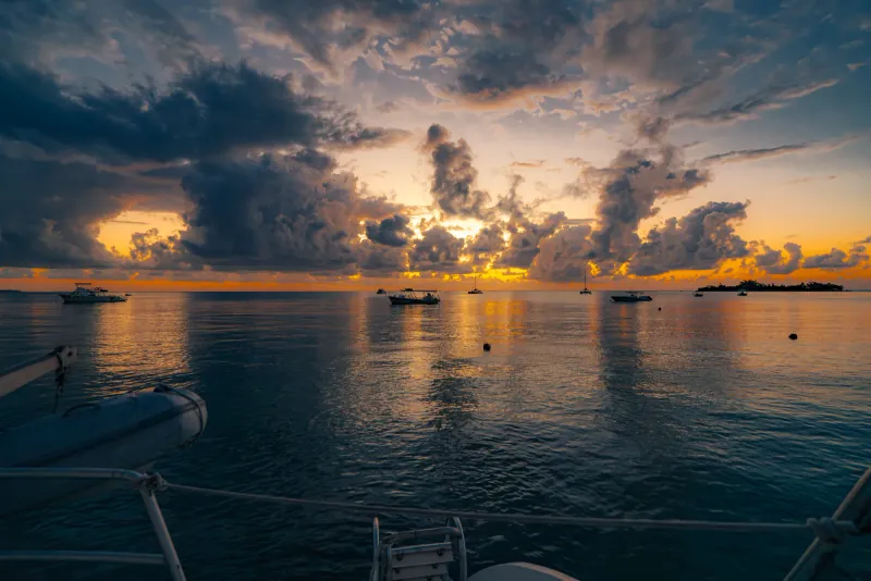 Boats moored on calm water beneath a dramatic orange and grey sunset sky