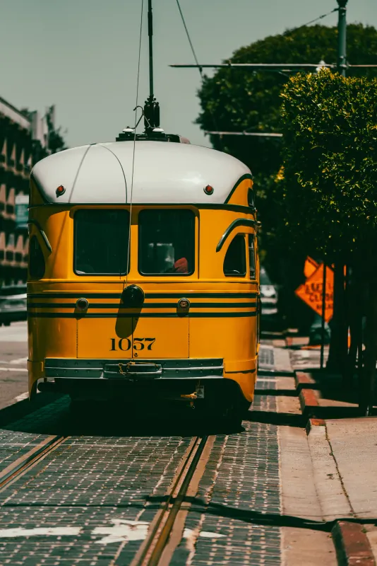 Yellow and white vintage streetcar number 1057 on tree-lined tracks in San Francisco