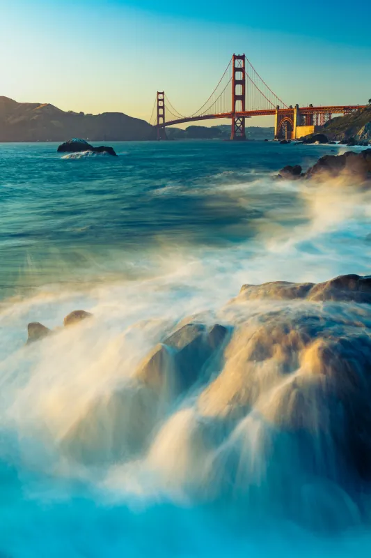 Silky waves washing over rocks with the Golden Gate Bridge in the distance