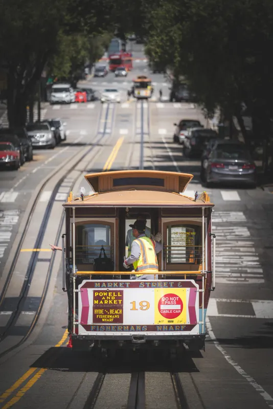 Rear view of a Powell and Market cable car with a gripman in a safety vest on a busy street