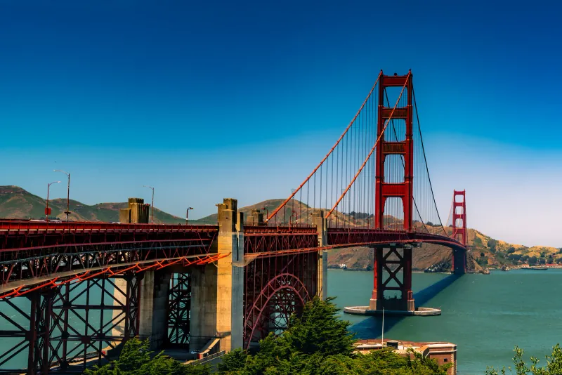 Golden Gate Bridge tower and red cables seen from the Fort Point side under clear skies