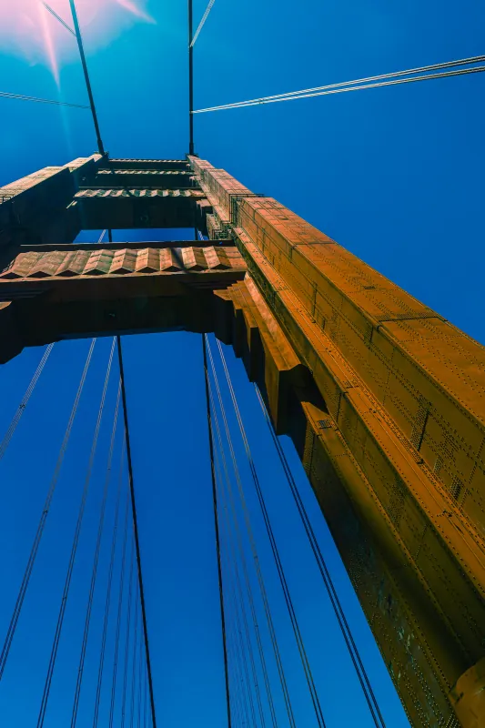 Looking straight up a Golden Gate Bridge tower and suspension cables against blue sky