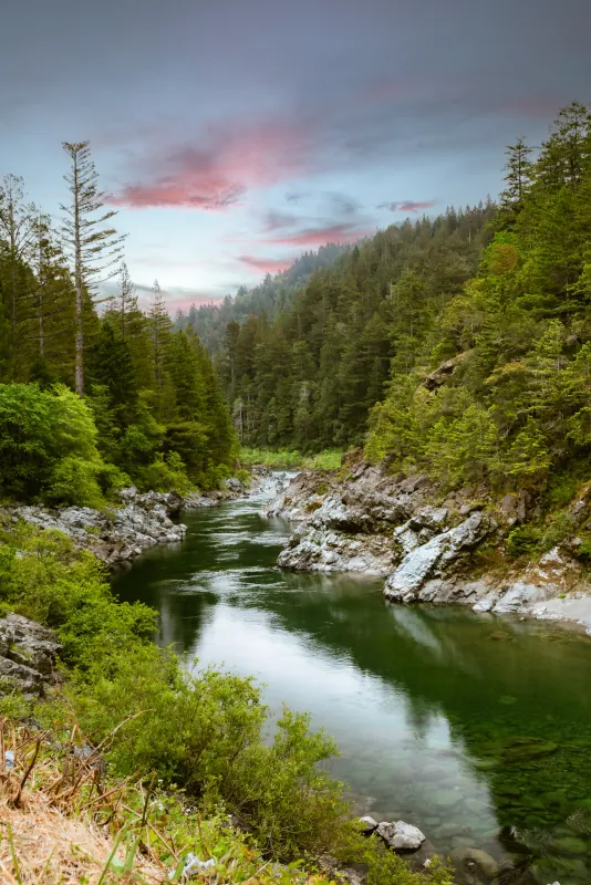 Emerald-green Smith River winding through a rocky forested canyon along Highway 199 in Northern California, pink evening sky above