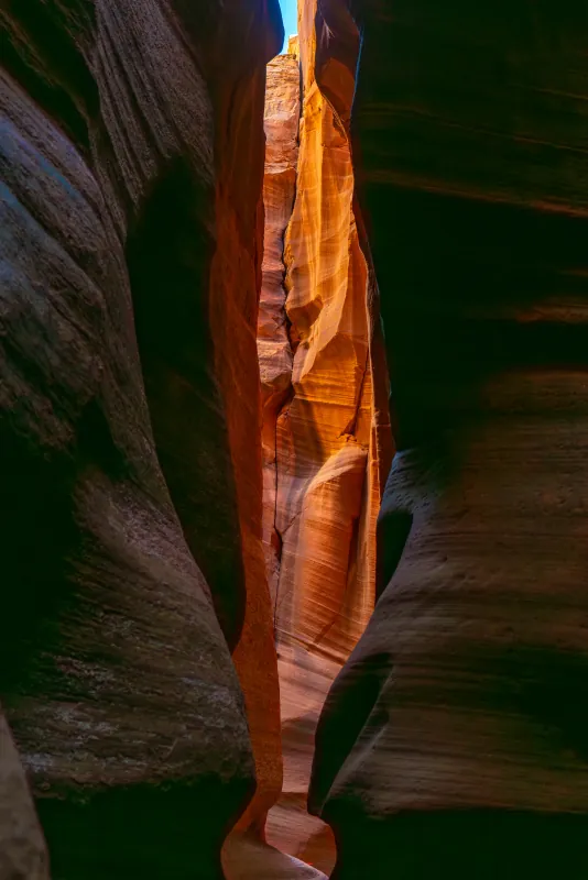 Narrow sandstone slot canyon glowing orange with a sliver of blue sky above