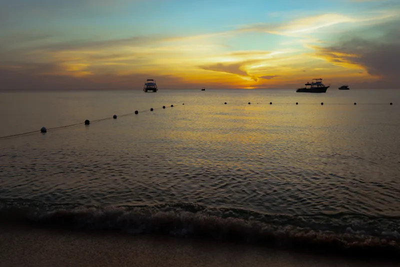 Buoy line stretching across calm water toward anchored boats under a golden sunset