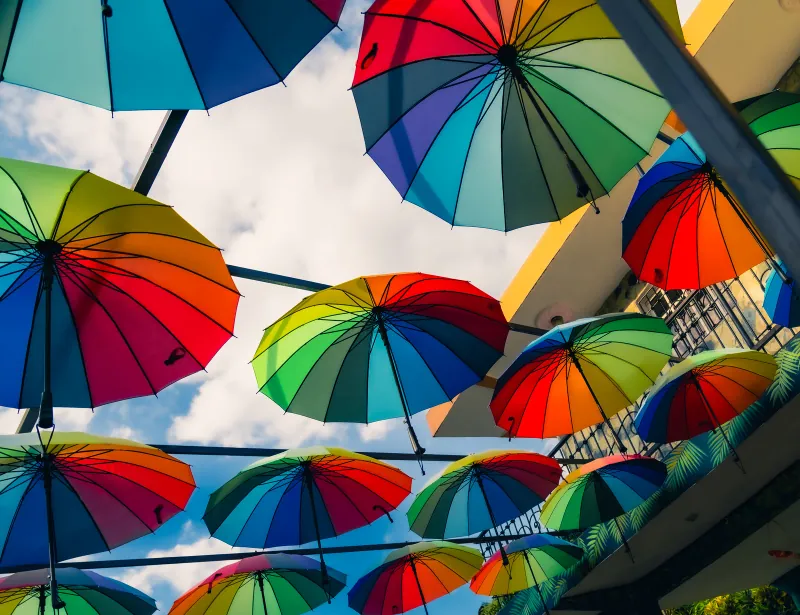 Rows of rainbow-striped umbrellas suspended overhead against a cloudy sky
