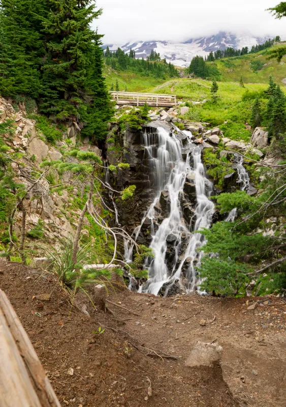 Waterfall tumbling below a footbridge with Mount Rainier's glaciers in the background