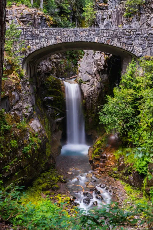Waterfall framed by a stone arch bridge in a mossy forest gorge